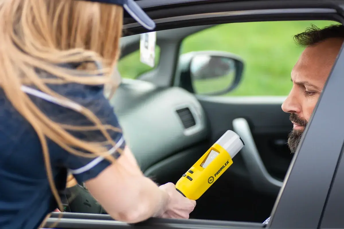 A police officer holds a yellow breathalyzer near a driver inside a car.