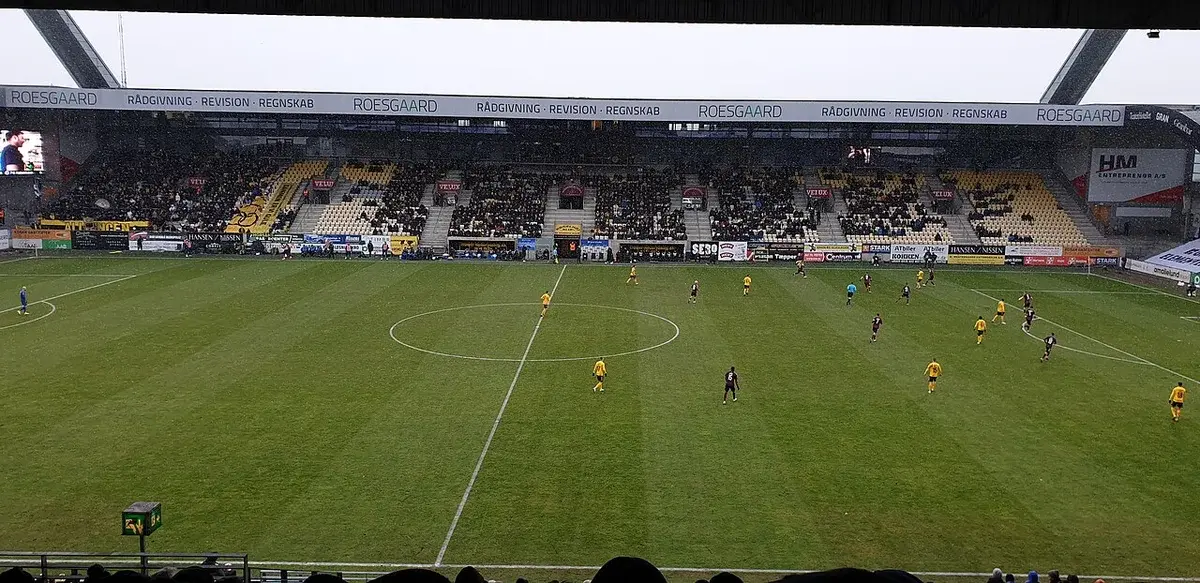 Wide view of a soccer match in a stadium with players on the field and crowd in the stands.