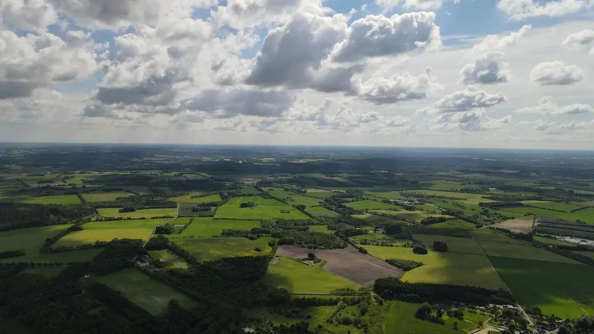 Aerial view of green farmland and rural fields under cloudy skies.