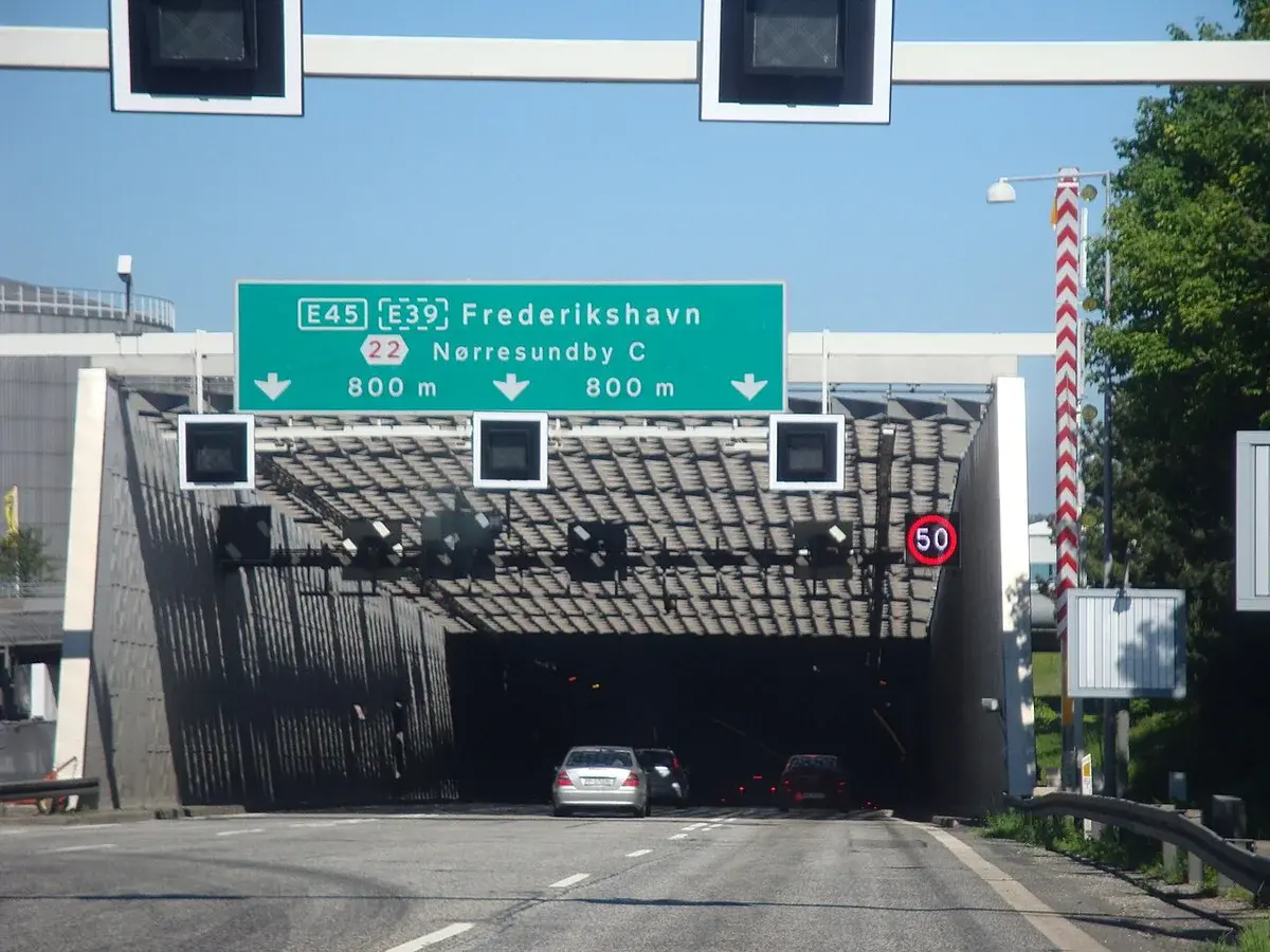 Road leading into a tunnel entrance in Denmark with overhead motorway signs.