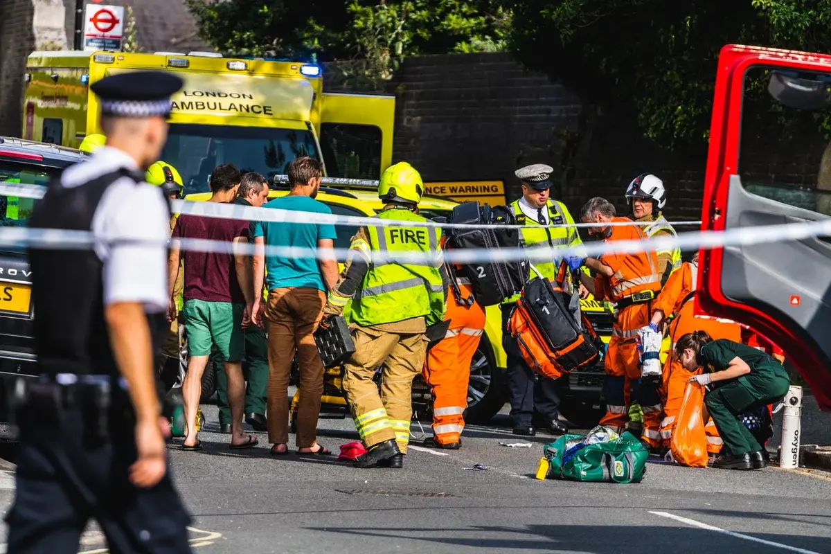 Firefighters, paramedics, and police respond to an incident beside a London Ambulance vehicle on a street.