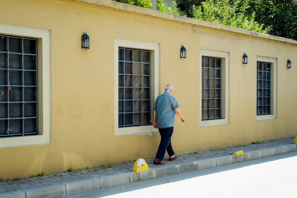 Elderly man walking beside a yellow wall with windows