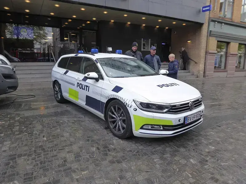 White police car parked on cobblestone street near building with people standing nearby