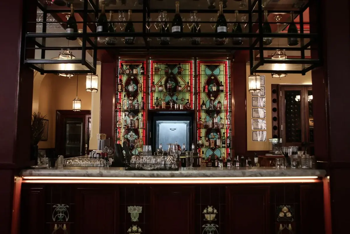 Elegant bar interior with stained glass panels, bottles, and glassware under warm lighting.